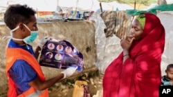 In this photo taken Wednesday, June 10, 2020, an internally-displaced Somali woman, right, is informed how to protect herself from the coronavirus, at the Weydow IDP camp in Mogadishu, Somalia. (Hamza Osman/International Organization for Migration (IOM) 