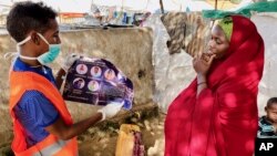 In this photo taken Wednesday, June 10, 2020, an internally-displaced Somali woman, right, is informed how to protect herself from the coronavirus, at the Weydow IDP camp in Mogadishu, Somalia. (Hamza Osman/International Organization for Migration (IOM) 