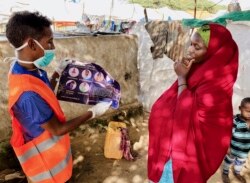 In this photo taken Wednesday, June 10, 2020, an internally-displaced Somali woman, right, is informed how to protect herself from the coronavirus, at the Weydow IDP camp in Mogadishu, Somalia. (Hamza Osman/International Organization for Migration (IOM)