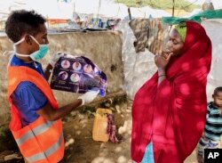 In this photo taken Wednesday, June 10, 2020, an internally-displaced Somali woman, right, is informed how to protect herself from the coronavirus, at the Weydow IDP camp in Mogadishu, Somalia. (Hamza Osman/International Organization for Migration (IOM)