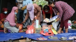 Para pengungsi akibat guguran awan panas Gunung Semeru, sedang memilah barang bantuan yang diberikan sesuai dengan kebutuhan mereka masing-masing di tenda pengungsian Desa Sumber Wuluh pada 8 Desember 2021. (Foto: VOA/Indra Yoga)