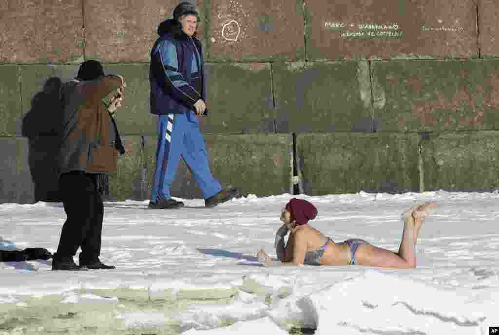 A man takes a photo of a woman who sunbathes on snow near the wall of St. Peter and Paul Fortress in St. Petersburg, Russia. The temperature in St. Petersburg is -12&deg; C (10&deg; F).