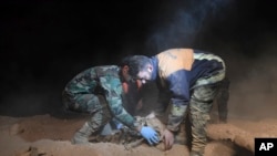 FILE - In this photo released by the Syrian official news agency SANA, Syrian security forces remove human remains at the site of two mass graves believed to contain the bodies of civilians and troops killed by Islamic State militants, in the village of Wawi near the northern city of Raqqa, Syria, Dec. 30, 2017. Nearly 50 bodies have been found in another recently discovered grave in Raqqa, a local official said April 21, 2018.