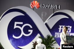 រូបឯកសារ៖ ស្ត្រីម្នាក់ឈរក្បែរផ្លាកសញ្ញា 5G នៃក្រុមហ៊ុន Huawei នៅក្នុងពិព័រណ៍បច្ចេកវិទ្យា PT Expo នៅទីក្រុងប៉េកាំង ប្រទេសចិន ថ្ងៃទី២៨ ខែកញ្ញា ឆ្នាំ២០១៨។