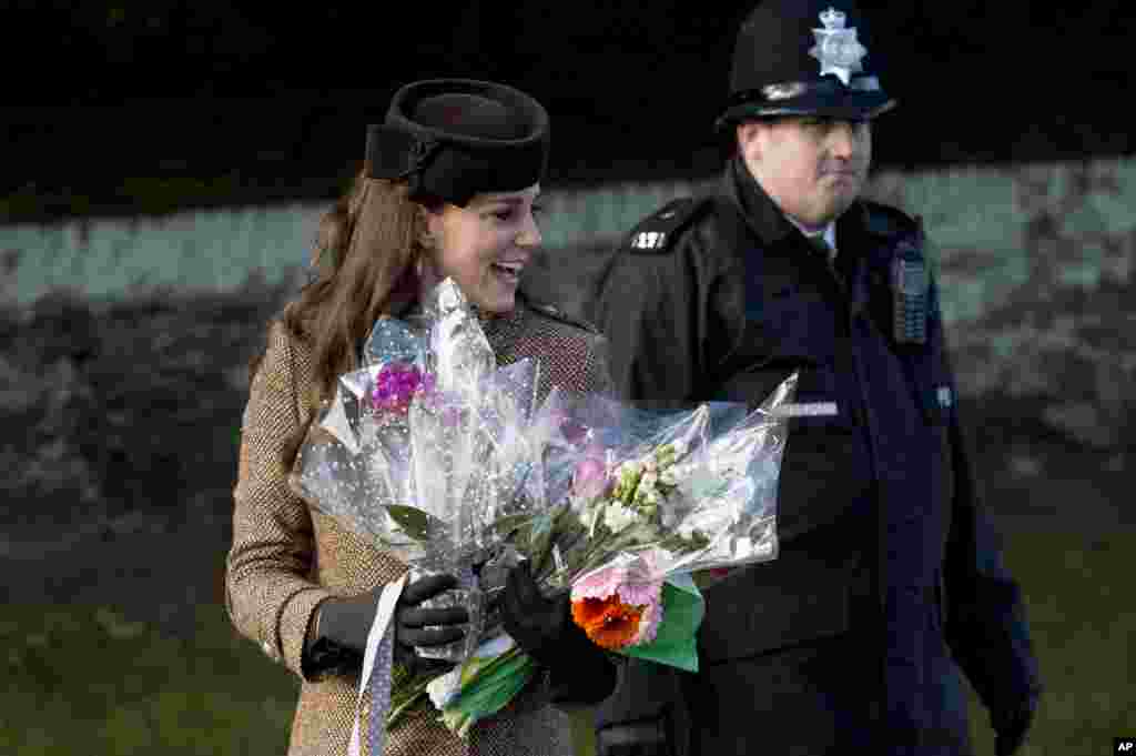 Putri Kate dari Cambridge, Inggris, memegang bunga yang diberikan oleh masyarakat yang berkumpul seusai menghadiri misa keluarga kerajaan Inggris di gereja Santa Maria Magdalena di Sandringham, Inggris (25/12).