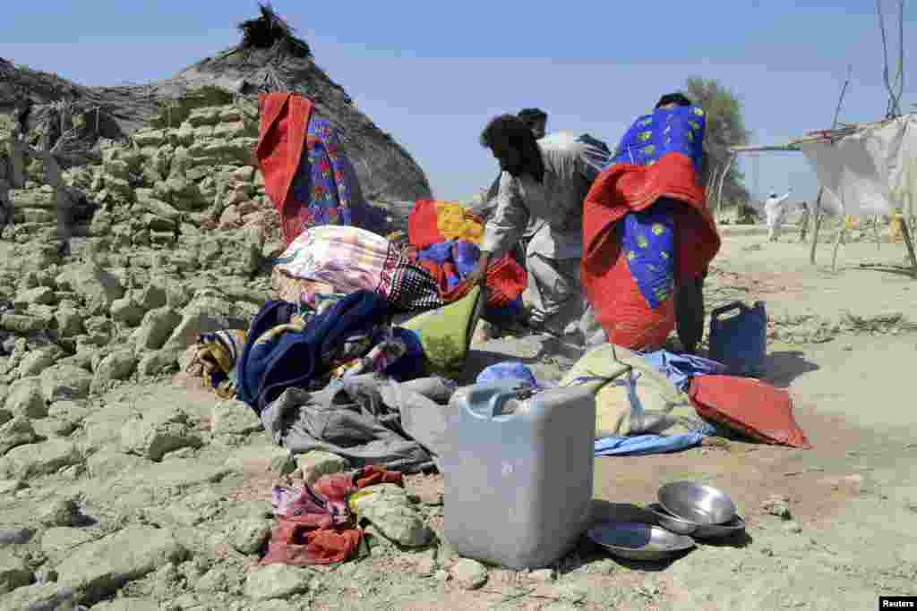 Para penyintas mengumpulkan barang milik mereka dekat reruntuhan rumah batako yang roboh akibat gempa di Awaran, Baluchistan. (Reuters/Naseer Ahmed)