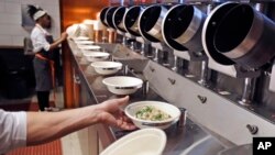 FILE - A worker lifts a lunch bowl off the production line at Spyce, a restaurant which uses a robotic cooking process, in Boston, Massachusetts, May 3, 2018.