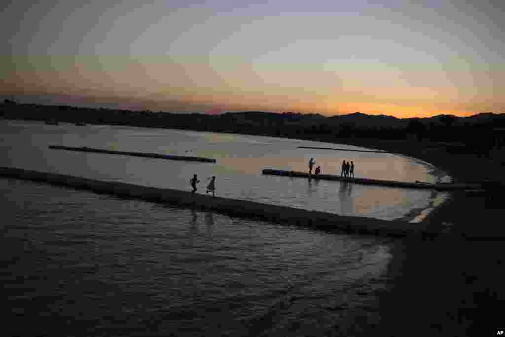 Workers repair a beach dock while kids run along as the sun sets at the Red Sea in the Sharm El Sheikh coastline resorts area, Egypt.