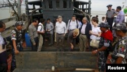 FILE - Myanmar government officials and U.N. officials stand on a boat used for human trafficking at a jetty outside Sittwe, Myanmar.