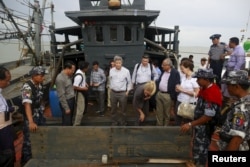 FILE - Myanmar government officials and U.N. officials stand on a boat used for human trafficking at a jetty outside Sittwe, Myanmar, May 23, 2015.