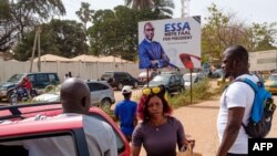 Des gens descendent d'un taxi près d'une grande affiche de soutien au candidat indépendant Essa Mbye Faal à Banjul le 29 novembre 2021 avant les élections présidentielles du 4 décembre 2021.