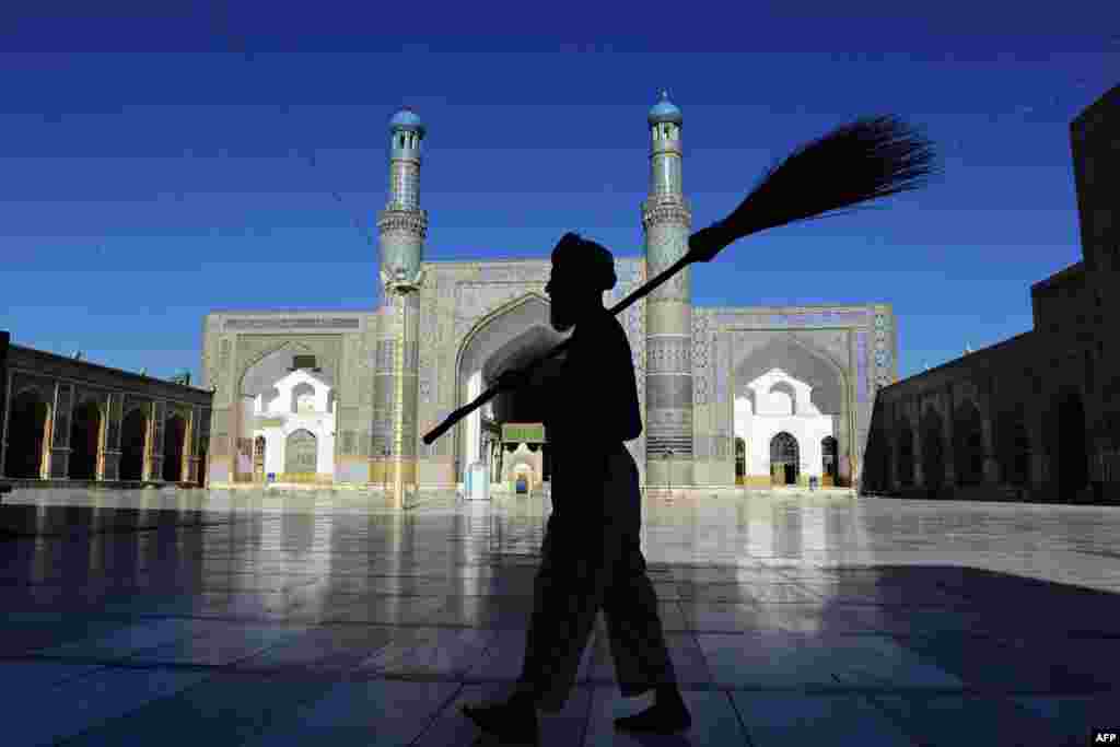 An Afghan sweeper carries his broom as he walks past the main mosque during the month of Ramadan in Herat, Afghanistan.