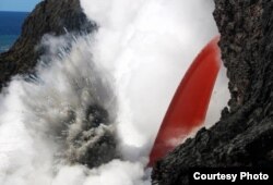 An open lava stream continues to pour out of the lava tube, perched high on the sea cliff, and into the ocean. The stream was remarkably steady today, but produced pulsating littoral explosions that threw spatter onto the sea cliff.