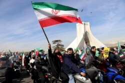 Seorang perempuan Iran melambaikan bendera kebangsaannya saat mengikuti pawai kendaraan bermotor dalam perayaan HUT ke-42 revolusi Islam di Teheran, Iran, 10 Februari 2021. (Majid Asgaripour/WANA via REUTERS)