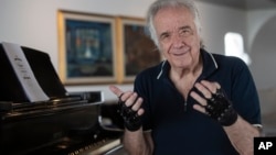 Brazilian pianist Joao Carlos Martins poses for pictures wearing bionic gloves at his home in Sao Paulo, Brazil, Wednesday, Jan. 22, 2020. (AP Photo/Andre Penner)
