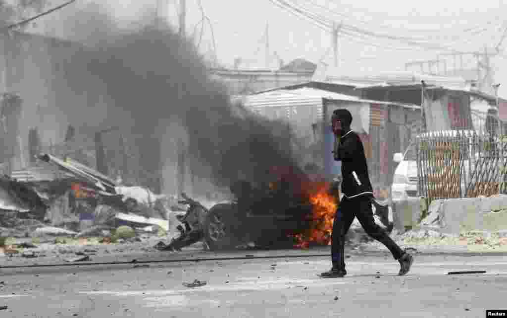 Mtu akizungumza kwa simu anapita mbele ya eneo la mlipuko wa bomu mbele ya mlango wa uwanja wa ndege wa mji mkuu wa Somalia capital Mogadishu, Feb. 13, 2014. 