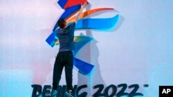 FILE - A crew member leaps to fix a logo for the 2022 Beijing Winter Olympics before a launch ceremony to reveal the motto for the Winter Olympics and Paralympics in Beijing, Sept. 17, 2021.