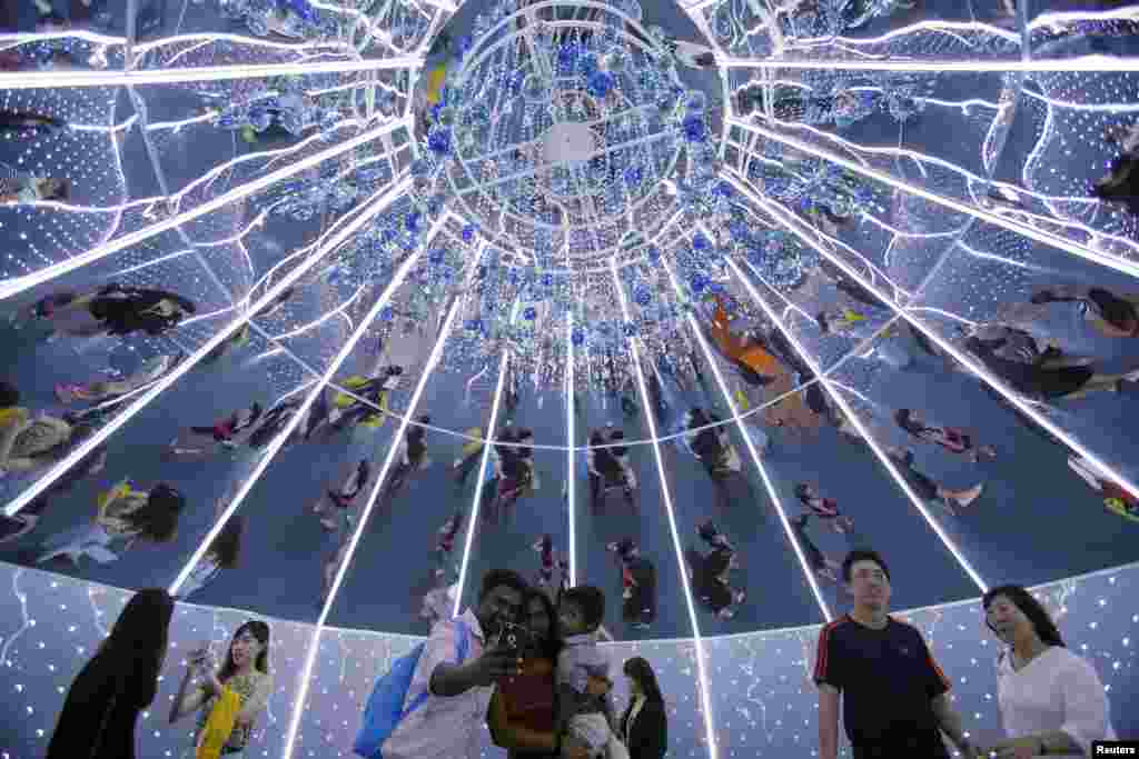 People are reflected in mirrors as they take photos inside a giant Christmas tree in the shopping district of Orchard Road in Singapore.