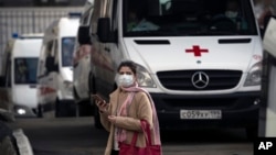 A woman wearing a face mask stands next to ambulances as they queue to transfer patients suspected of having the coronavirus infection to a hospital in Moscow, Russia, Thursday, April 9, 2020.