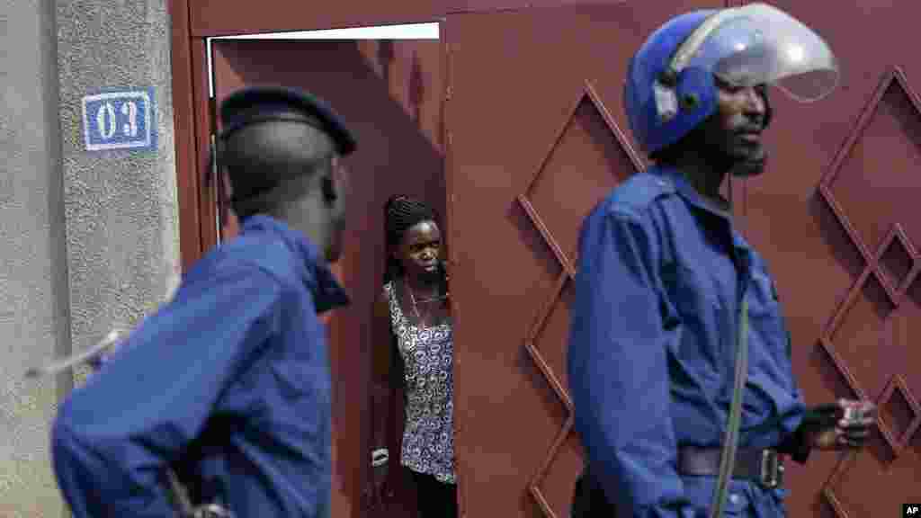 A woman looks out of her house as riot police walk by in the Nyakabiga district, Bujumbura, May 4, 2015.