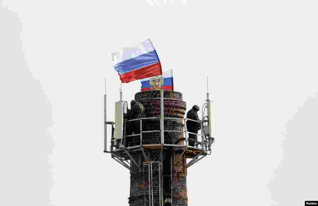 Pria bersenjata, diyakini sebagai tentara Rusia, berdiri di atas cerobong asap dekat markas besar angkatan laut, dengan bendera Rusia dikibarkan di dekat markas tersebut, di Sevastopol, 19 Maret 2014.