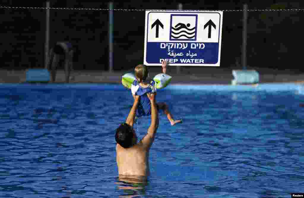 An Israeli man holds his son in the pool at Kibbutz Yad Mordechai, near the border with northern Gaza, Aug. 6, 2014.