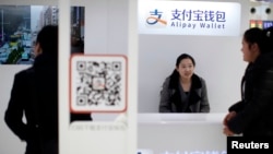 FILE - A sales assistant sits behind and under Alipay logos at a train station in Shanghai, Feb. 9, 2015. Apple Pay has joined China's fast-growing mobile payment market and is challenging two major local brands, Alipay and WeChat Wallet.