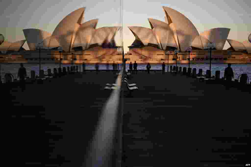 Sunset hues fall on the landmark Sydney Opera House as it is seen in a reflection from Circular Quay, usually packed with tourists, in Sydney, Australia.