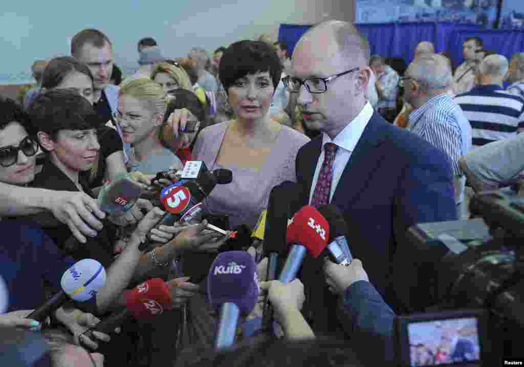 Ukraine&#39;s Prime Minister Arseny Yatseniuk (R) accompanied by his wife Teresiya (C) speaks to journalists after voting in a presidential election at polling station in Kyiv.