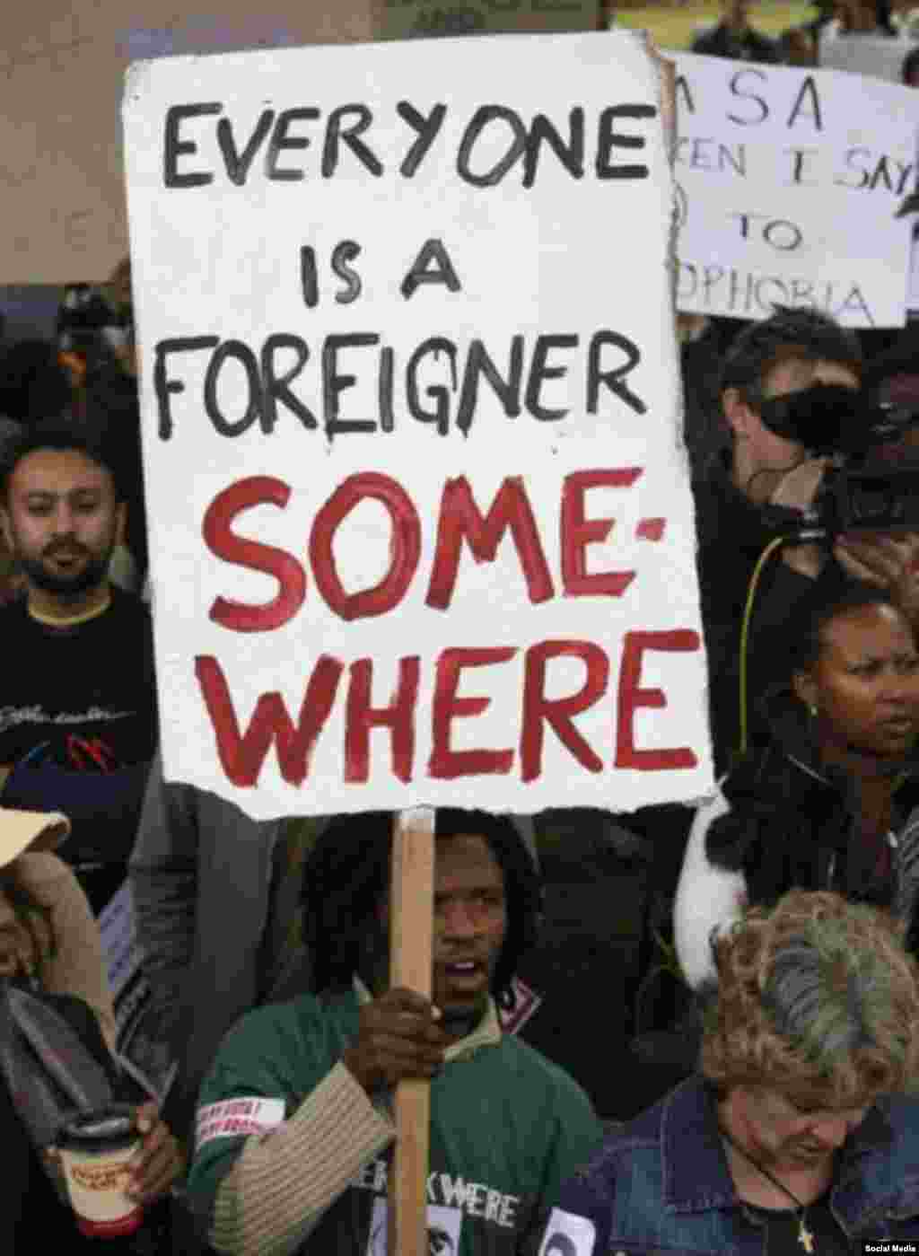 Grupo protesta a violência com uma placa que diz &quot;Somos todos imigrantes em algum lugar&quot;