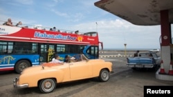 FILE - A vintage car carrying tourists waits in line to fill up with fuel at a gas station as a tourist bus passes by along the seafront boulevard "El Malecon" in Havana, January 12, 2015. 
