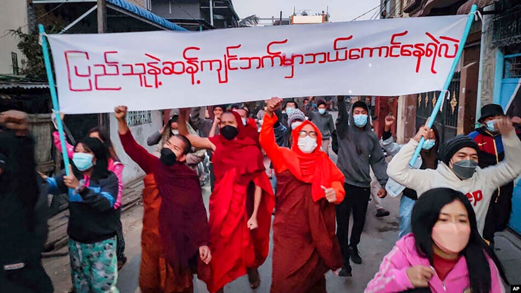 Youth activists and Buddhist monks participate in an anti-military government protest rally while holding a banner that reads in Burmese, "Who dares to stay on the opposite side of the people's will," on Tuesday, Feb. 1, 2022, in Mandalay, Myanmar. The ne