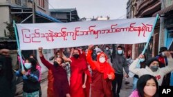 Youth activists and Buddhist monks participate in an anti-military government protest rally while holding a banner that reads in Burmese, "Who dares to stay on the opposite side of the people's will," on Tuesday, Feb. 1, 2022, in Mandalay, Myanmar. The ne