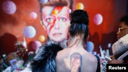 A woman with a Ziggy Stardust tattoo visits a mural of David Bowie in Brixton, south London, Jan. 11, 2016. 