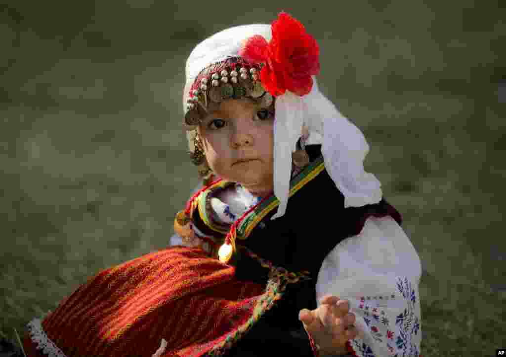 Kristina, bé gái người Bulgaria 2 tuổi, mặc trang phục truyền thống ngồi trên bãi cỏ trong một đám cưới ở Pchelina, Bulgaria, ngày 6 tháng 7, 2014.