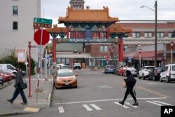 Pedestrians walk near the main entrance to Seattle's Chinatown-International District Thursday, March 18, 2021. (AP Photo/Ted S. Warren)