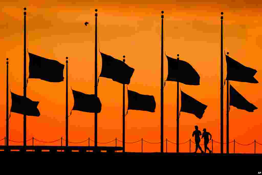 Runners pass under the the flags flying at half-staff around the Washington Monument at daybreak in Washington. The flags were ordered to half-staff by President Barack Obama to honor the victims of the Orlando nightclub shootings.