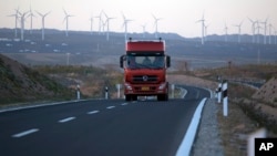 FILE - A truck travels down a highway with wind turbines in the background in northwestern China's Ningxia Hui autonomous region, Oct. 9, 2015.