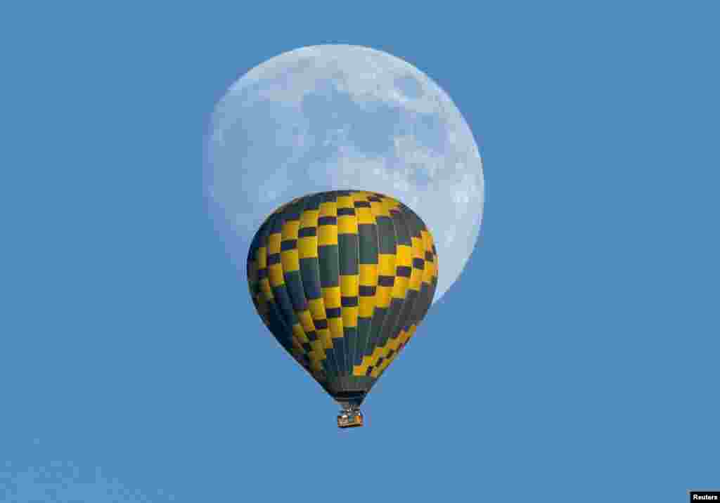 A hot air balloon floats past an almost-full rising moon on a warm fall evening near Encinitas, California, USA. 