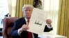 President Donald Trump holds up the $1.5 trillion tax overhaul package he signed in the Oval Office of the White House in Washington, Dec. 22, 2017.