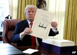 President Donald Trump displays the $1.5 trillion tax overhaul package he had just signed, Friday, Dec. 22, 2017.