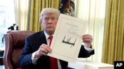 President Donald Trump holds up the $1.5 trillion tax overhaul package he signed in the Oval Office of the White House in Washington, Dec. 22, 2017.