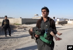 FILE - An Afghan man carries a wounded girl at the side of a suicide attack that killed civilians and a policeman in Lashkar Gah, the capital of Helmand province, south of Kabul, Afghanistan, March 16, 2015.