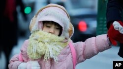 Seorang anak perempuan dengan pakaian tebal dan berlapis memegang tangan ibunya dalam perjalanan ke sekolahnya di New York (8/1/2015).