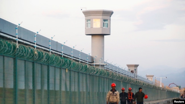 资料图片：几名工人在新疆一再教育营外走过。