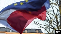 An unseen protester waves the flags of Poland and the European Union in front of the Polish Constitutional Court after a sentence regarding the appointment of judges, Warsaw, Dec. 3, 2015. 