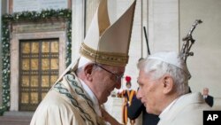 Le pape François, à gauche, donne une accolade au pape émérite Benoît XVI, à droite, avant d’ouvrir la Porte Sainte, vu dans l’arrière-fond, au cours d'une cérémonie marque le début de l'Année sainte, au Vatican, 8 décembre 2015.