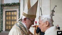 Le pape François, à gauche, donne une accolade au pape émérite Benoît XVI, à droite, avant d’ouvrir la Porte Sainte, vu dans l’arrière-fond, au cours d'une cérémonie marque le début de l'Année sainte, au Vatican, 8 décembre 2015. 