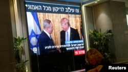 A woman reads a newspaper as monitors showing the meeting between U.S. President Donald Trump and Israeli Prime Minister Benjamin Netanyahu in Washington, are seen next to a coffee shop in Tel Aviv, Israel, Feb. 15, 2017.