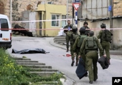 FILE - In this Thursday, March 24, 2016 file photo, Israeli soldiers stand near the body of a Palestinian who was shot and killed by a soldier while laying wounded on the ground after a stabbing attack in Hebron, West Bank.